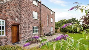 A brick building with a wooden door, windows, and a paved patio with benches. - 7 bedroom accommodation in Blackden, near Crewe (Blackden, near Crewe)