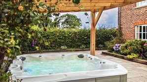 A hot tub under a wooden pergola in a garden with a brick building in the background. - 7 bedroom accommodation in Blackden, near Crewe (Blackden, near Crewe)
