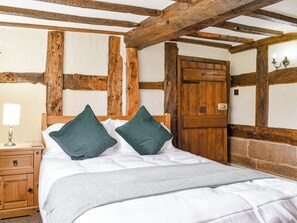 Un dormitorio con una cama de madera, dos almohadas, una mesita de noche con una lámpara y una puerta de madera.