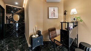 A modern hotel room with a marble floor, a black-framed mirror, a framed picture on the wall, a desk with a lamp, and a brown leather chair. - Clyde Athens by Nin&Bau (Athens)