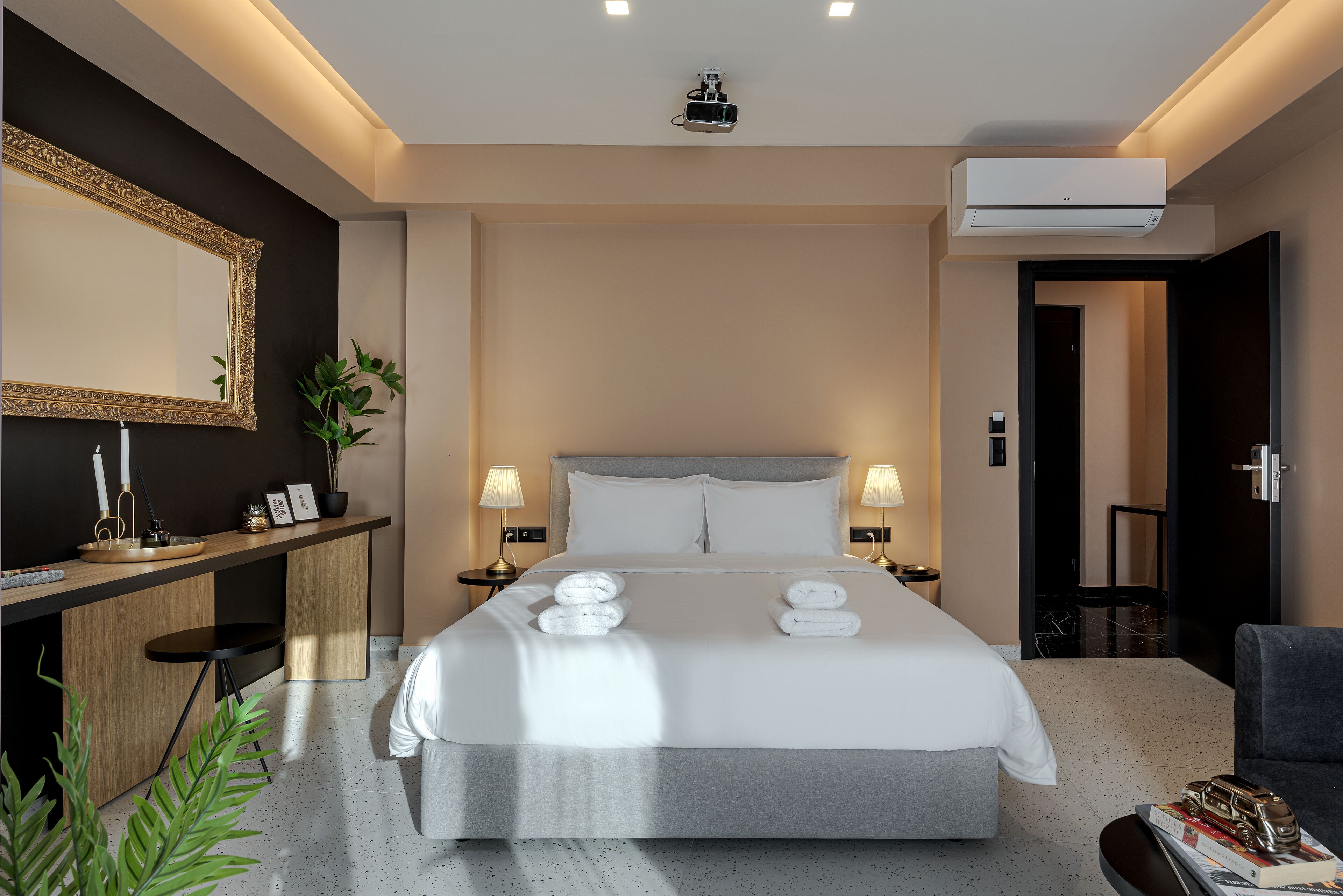 Una habitación de hotel moderna con una cama grande, lámparas de noche, un escritorio con espejo y una pequeña planta.