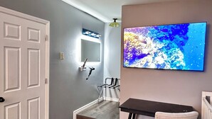 Ein Flur mit einer weißen Tür, einem kleinen Tisch mit Stuhl, einem wandmontierten Fernseher und einem Spiegel.