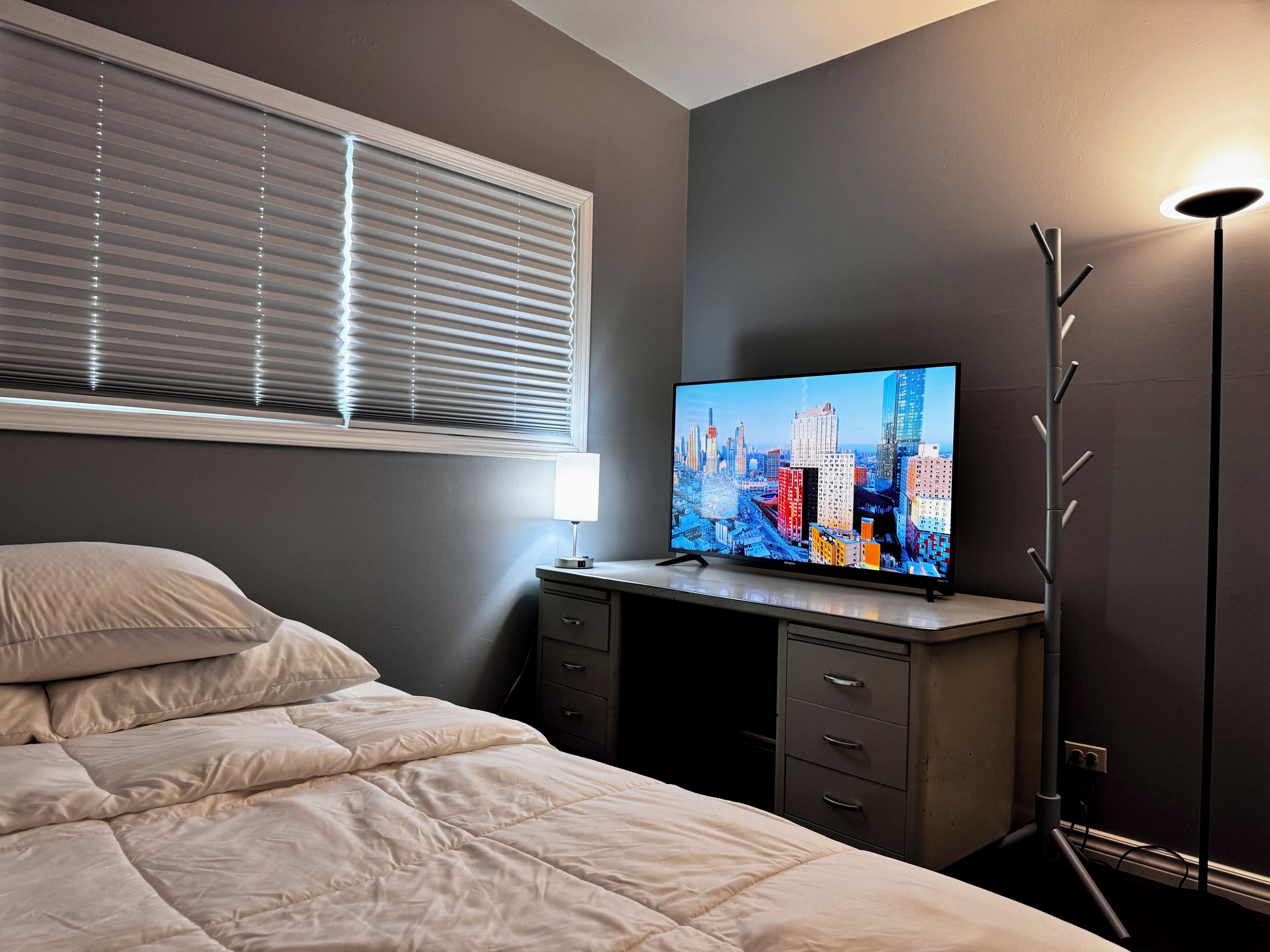 Quarto com cama, escrivaninha com televisão, luminária e abajur.