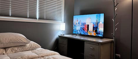 Quarto com cama, escrivaninha com televisão, luminária e abajur.