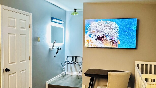Ein Schlafzimmer mit einem Bett, einem Schreibtisch, einem Stuhl, einem Babybett, einem Fernseher und einem Spiegel.