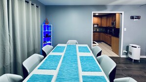 Ein Essbereich mit Tisch und Stühlen, einem blauen Teppich, einem weißen Schrank und einer durchgehenden Tür erkennbaren Küche.