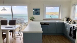 Una cocina moderna con una isla grande, vistas al océano y un comedor con mesa y sillas.