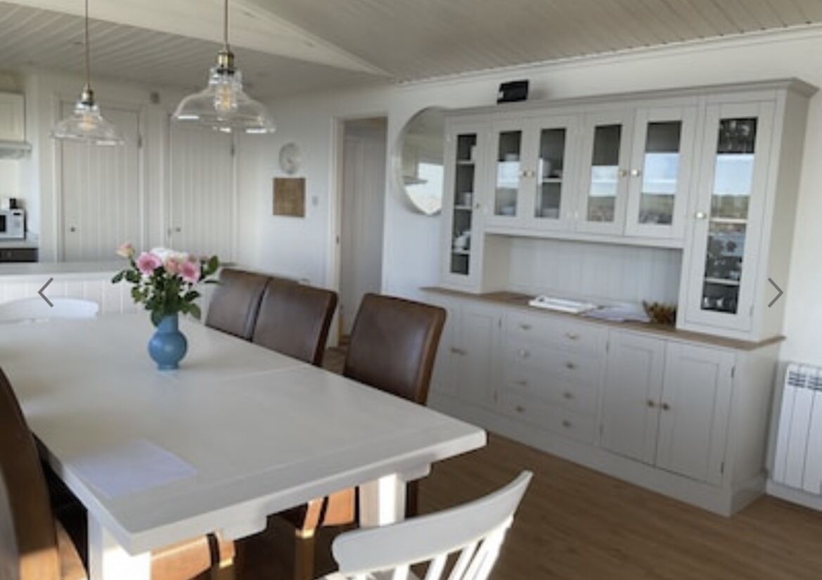 A dining area with a white table, brown chairs, and a vase with flowers. There are white cabinets with glass doors and a white ceiling.