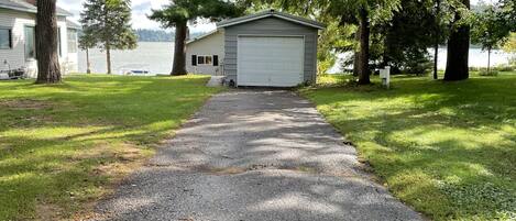 A gravel driveway leading to a garage with a white door, surrounded by trees and a lake view.