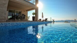 An infinity pool with clear blue water, a covered seating area with chairs and a table, and a view of the mountains in the background. - Penthouse with excellent sea views (Brsec)