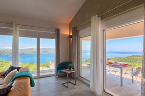 A spacious living room with a large sliding glass door leading to a balcony with a table and chairs, overlooking a scenic view of a body of water and greenery. - Penthouse with excellent sea views (Brsec)