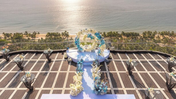 A rooftop terrace with a circular floral arrangement and tables, overlooking a beach and ocean. - Kalia Hotel (Phu Quoc)