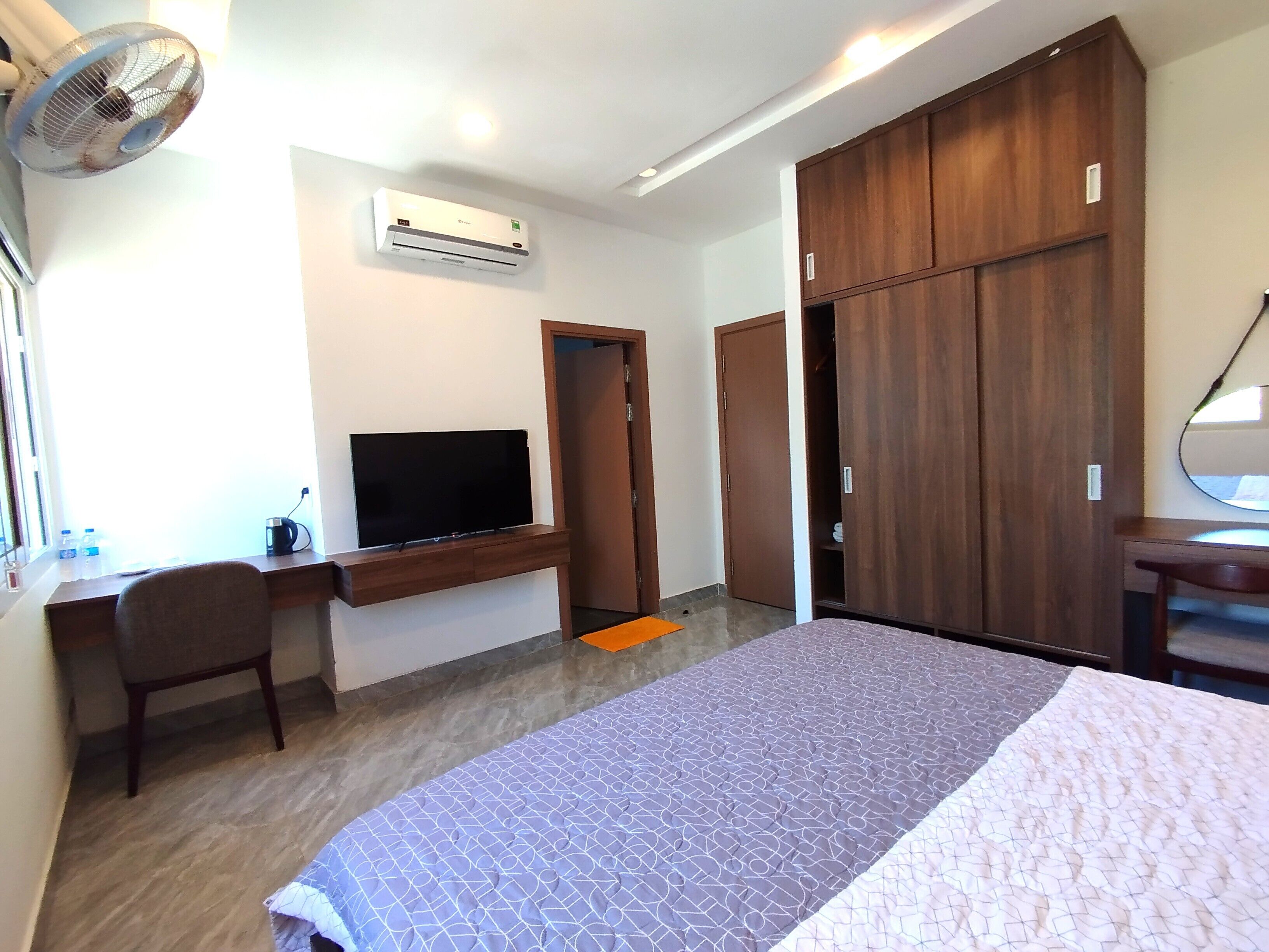A bedroom with a bed, a desk with a TV, a wardrobe, and an air conditioner.