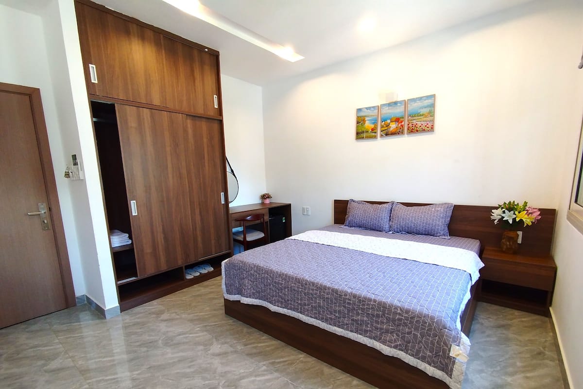 A bedroom with a bed, a wardrobe, a desk, and a wall-mounted artwork.