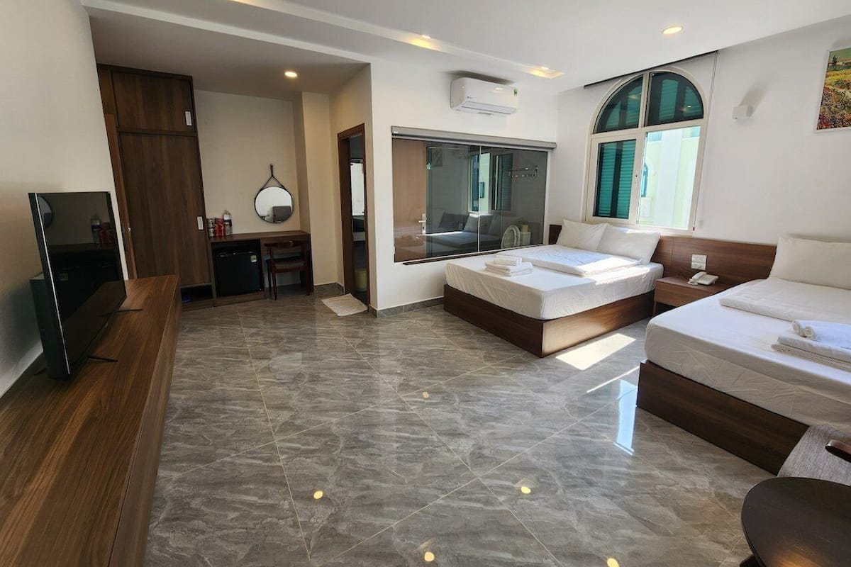 A modern hotel room with a large bed, a desk, a television, and a bathroom with a glass shower.