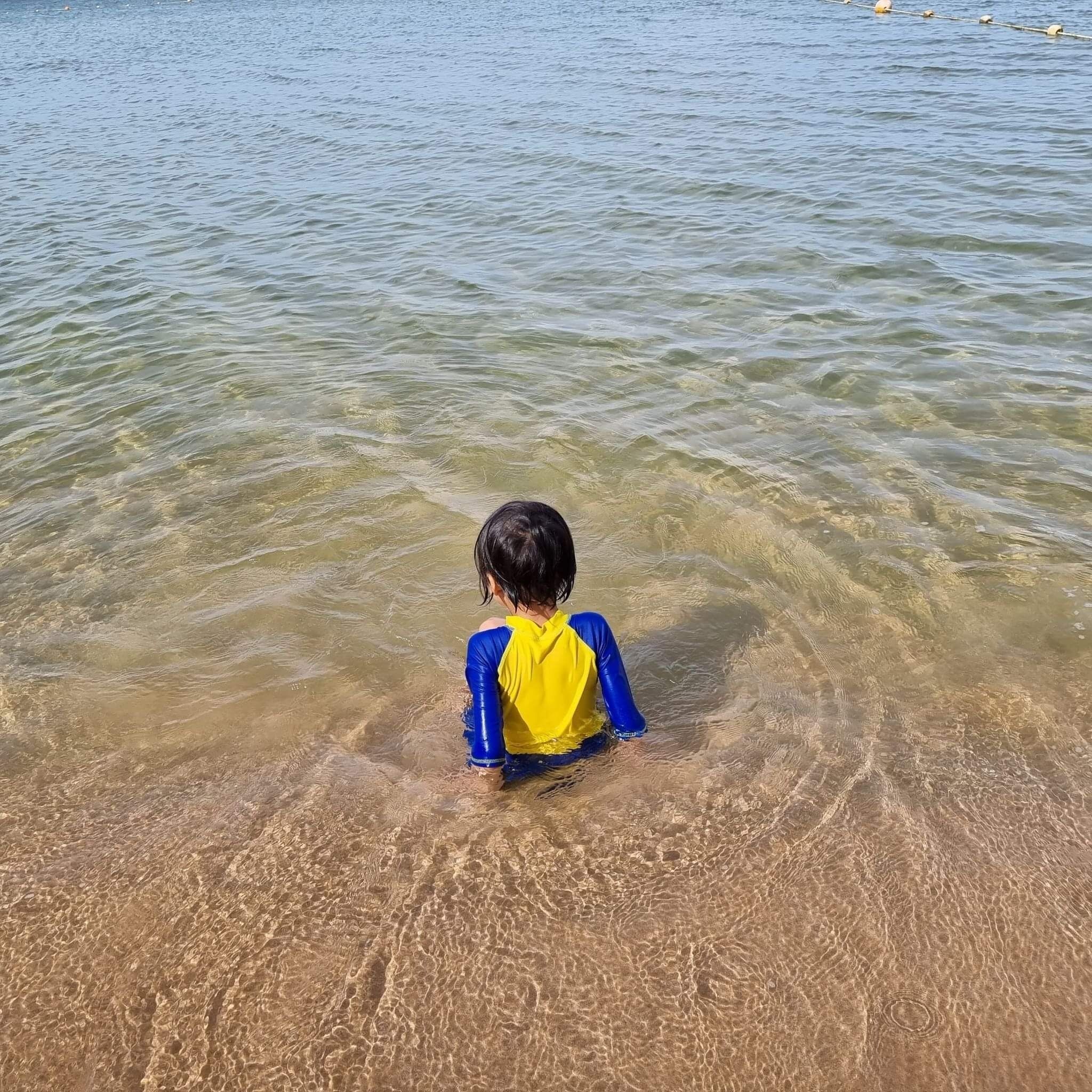 A child in a blue and yellow swimsuit standing in shallow water.