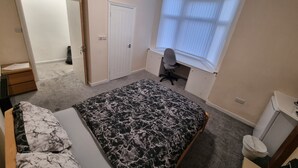 Quarto com cama, escrivaninha e janela.