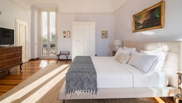 A bedroom with a large bed, a dresser, a television, and a door leading to a balcony.