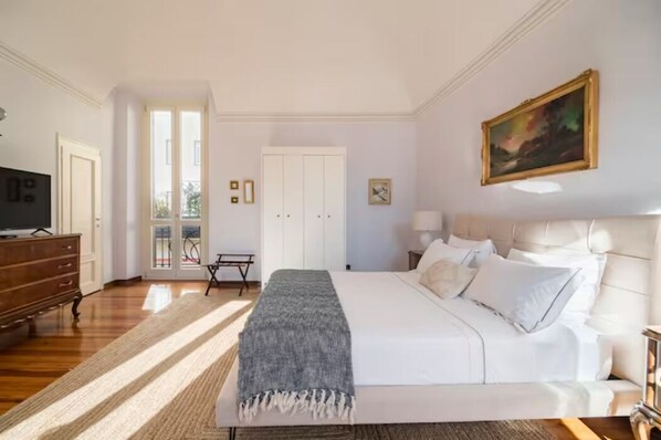 Ein Schlafzimmer mit einem großen Bett, einem Schminktisch, einem Fernseher und einer Tür, die auf einen Balkon führt.