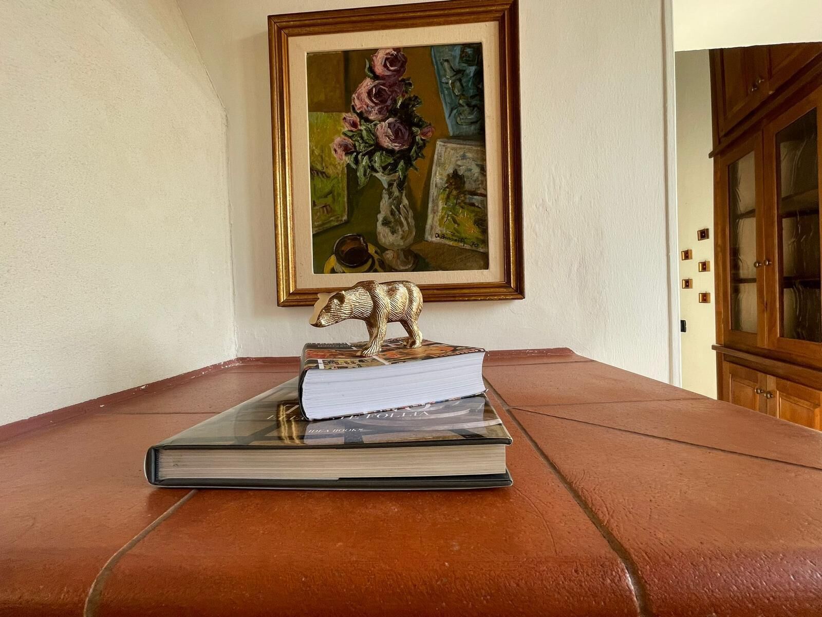 A book with a bear figurine on top, placed on a table with a framed painting above it.