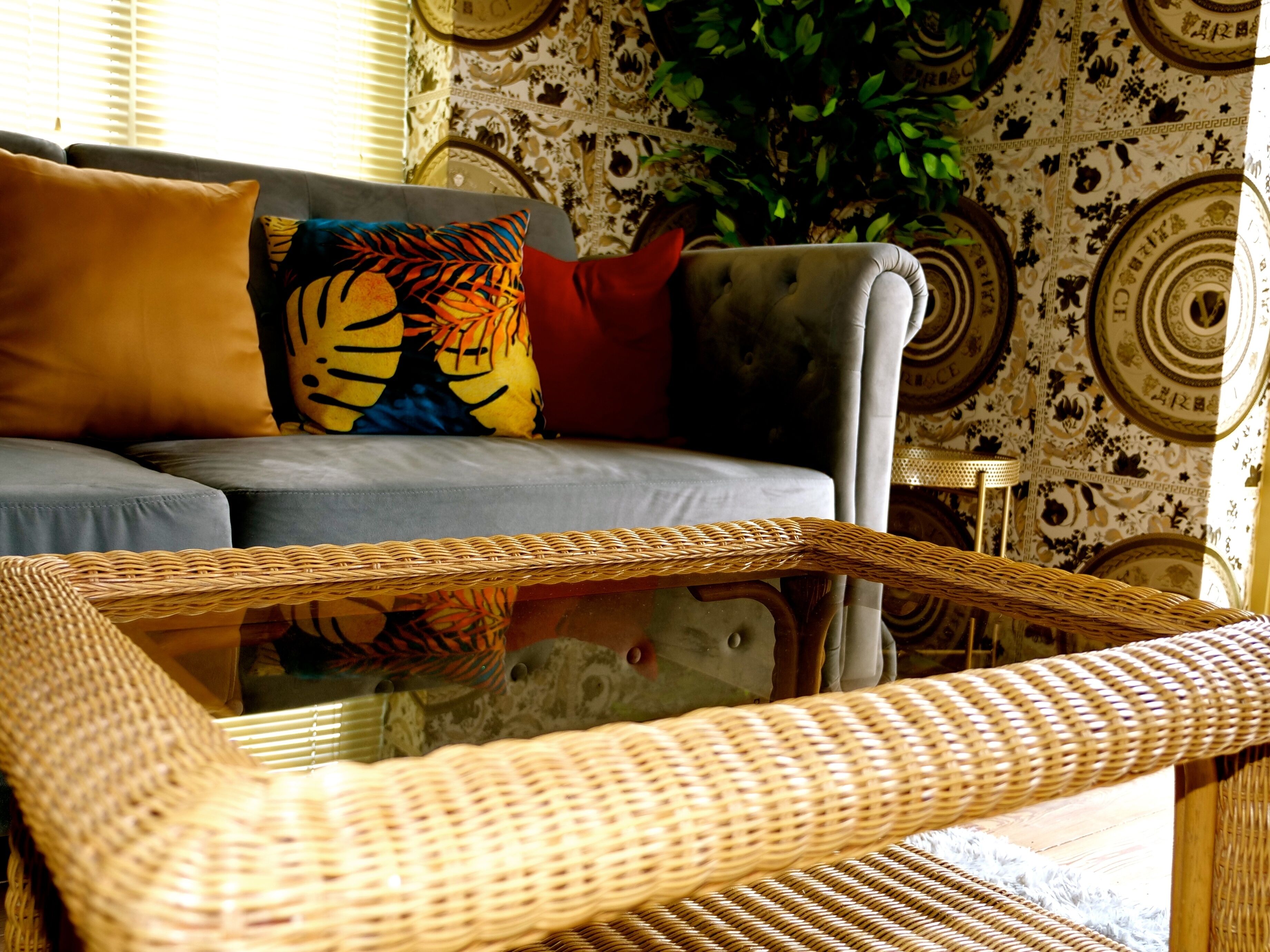 A living room with a sofa, colorful pillows, a wicker coffee table, and a patterned wall.