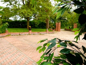 Un sendero pavimentado en un jardín, con bordes de ladrillo, rodeado de abundante vegetación y árboles.