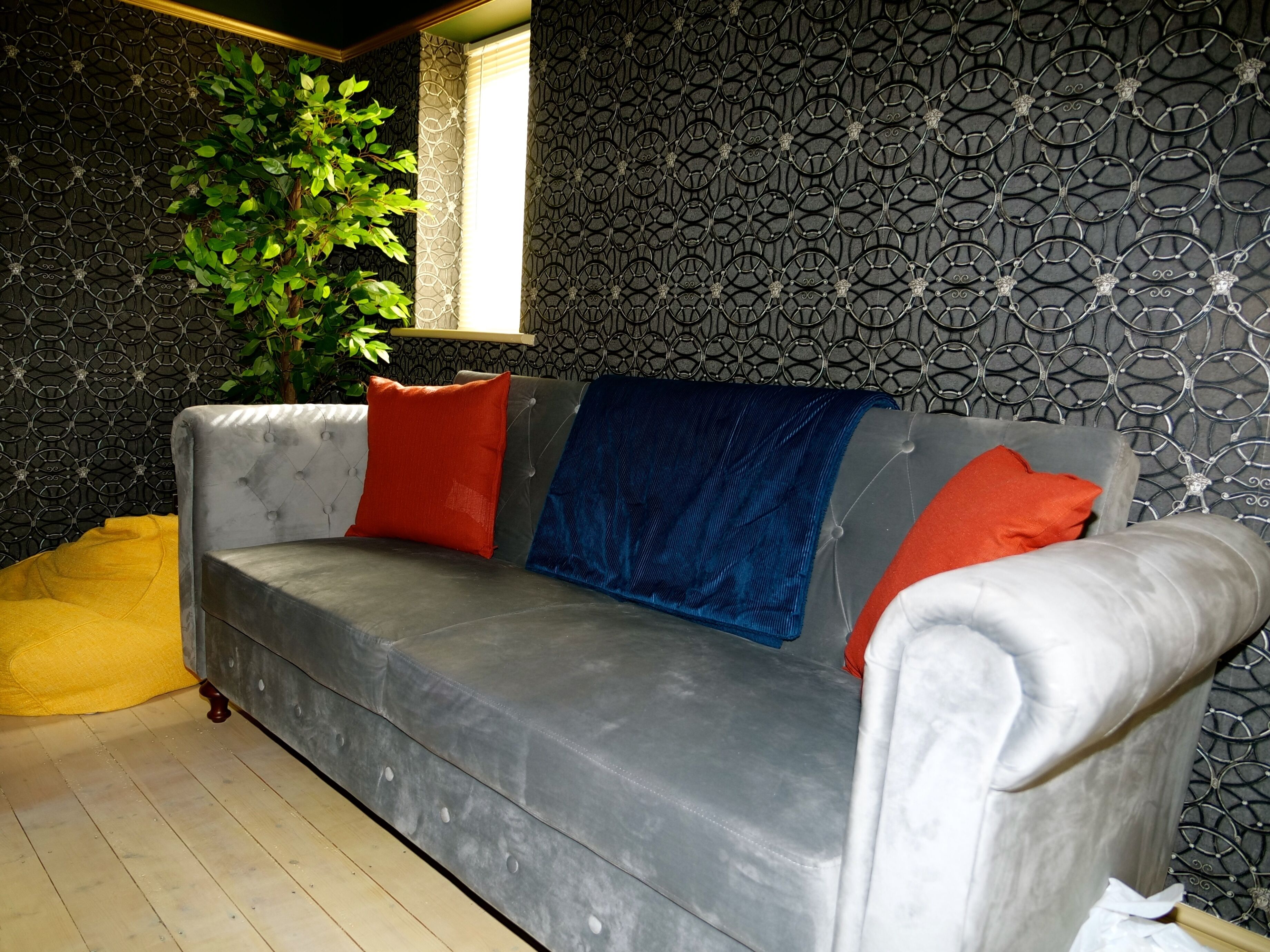 A grey sofa with red and blue cushions, a yellow bean bag, and a patterned wall.