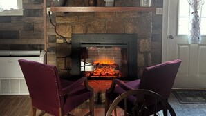 Une pièce chaleureuse avec une cheminée, un plafond en bois et deux fauteuils violets.
