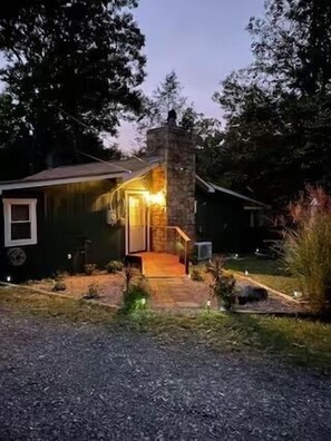 Una casa con chimenea de piedra, un porche de madera y un camino de entrada de grava.