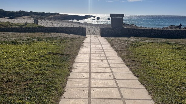 A pathway leading to a beach with a stone wall on either side.