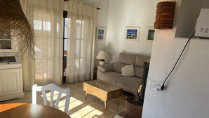 A cozy living room with a sofa, a wooden coffee table, and a dining table with chairs. There is a kitchen area with a stove and a refrigerator.
