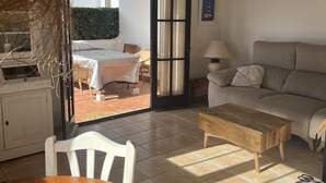 A cozy living room with a sofa, a wooden coffee table, and a dining table with chairs. There is a sliding glass door leading to an outdoor patio area with a table and chairs.