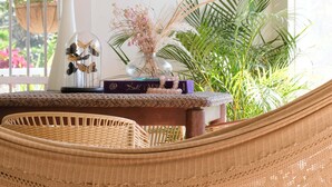 Una habitación con una silla de mimbre, una jaula de pájaros y una planta en maceta.