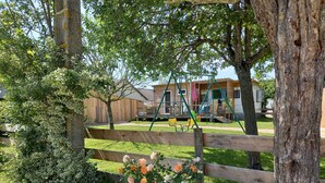 A wooden fence, a swing set, and a building with a deck in the background. - Bungalow on a horse farm (Yèvres)