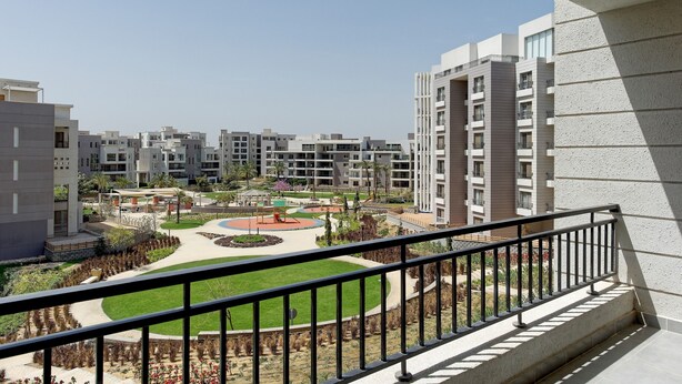 Un complejo residencial con edificios modernos, un patio central con jardín circular y barandilla de balcón.