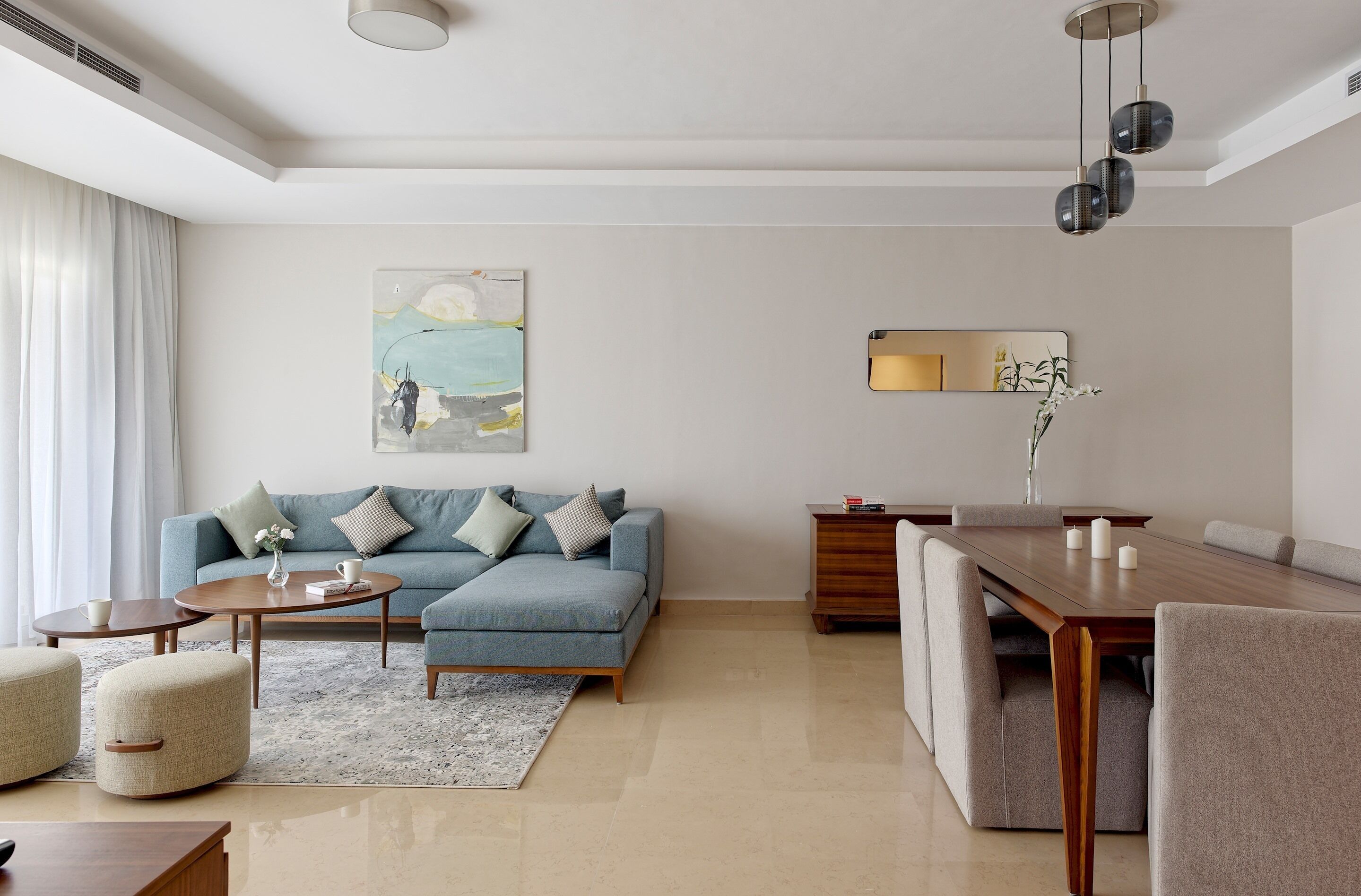 A modern living room with a sofa, coffee table, ottoman, and dining area with a wooden table and chairs.