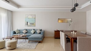 Una sala moderna con sofá, mesa de centro, reposapiés y comedor con mesa y sillas de madera.