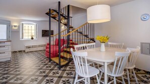 A modern kitchen with a central island, a dining area with white chairs, a staircase with a black railing, and a large pendant light. - Impeccable 4-bed Apartment in Osor (Mali Losinj)