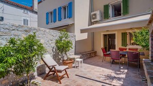 A courtyard with a stone wall, a wooden chair, a table with chairs, and a potted plant. - Impeccable 4-bed Apartment in Osor (Mali Losinj)