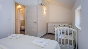A bedroom with a bed, a crib, a dresser, and an air conditioning unit. - Impeccable 4-bed Apartment in Osor (Mali Losinj)