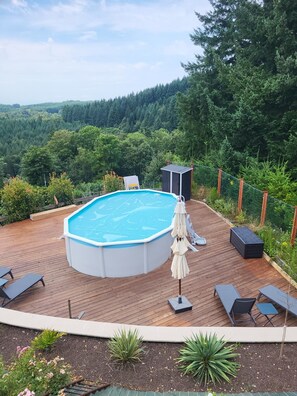 Une piscine extérieure dotée d’une terrasse en bois, entourée d’une végétation luxuriante et bordée par une forêt.