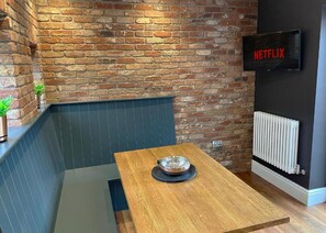 Un rincón acogedor con una mesa de madera, un cuenco de metal y una pared de ladrillo.