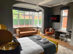 Una habitación de hotel moderna con una cama grande, un sofá, un escritorio y un televisor que muestra 'NETFLIX'.