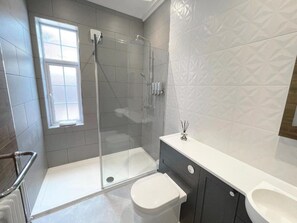 Un baño moderno con ducha de vidrio, inodoro blanco y tocador con espejo.