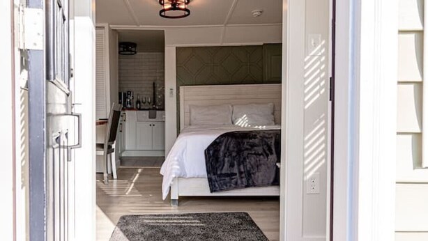 A bedroom with a bed, a bedside table, and a nightstand. There is a window with blinds and a door leading to the outside. - Cozy Cabin in a rural setting #10 In Temple, NH (Temple)