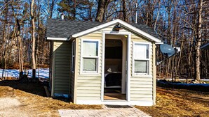 A small, single-story shed with a door open, revealing a bed inside. - Cozy Cabin in a rural setting #10 In Temple, NH (Temple)