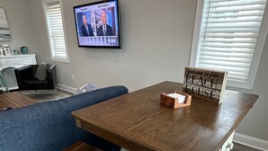Un salon moderne avec une table à manger en bois, deux bancs assortis, un téléviseur fixé au mur et une pancarte sur laquelle on peut lire : « Bienvenue dans notre maison de vacances en bord de mer ».