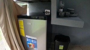 Une petite cuisine équipée d’un réfrigérateur, d’un four à micro-ondes et d’une petite étagère où sont rangés les ustensiles de cuisine.