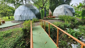 Deux structures en forme de dôme géodésique, situées dans un jardin luxuriant, avec un sentier verdoyant et des bancs en bois.
