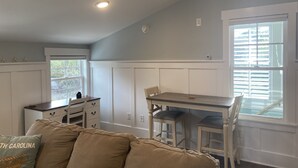 A room with a dining table, chairs, a sofa, and a window with blinds. - 4-minute walk to beautiful Emerald Isle beach access. (Emerald Isle)